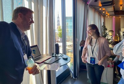 wei Personen unterhalten sich lachend an einer Station mit einem KI-Voice-Agent.