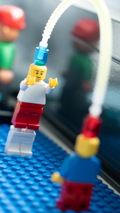 Lego Serious Play Workshop Köpfe: Nahaufnahme von zwei Lego-Figuren, die durch ein transparentes Rohr miteinander verbunden sind.