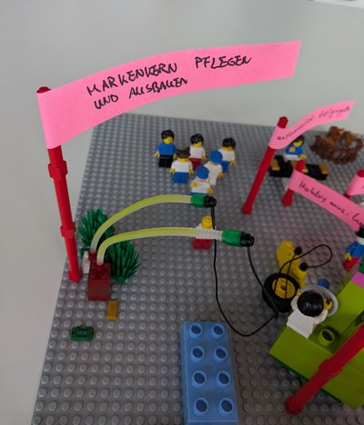 Lego Serious Play Workshop Markenkern: Ein aus Lego gebautes Modell, das eine Botschaft auf einem pinkfarbenen Zettel darstellt.