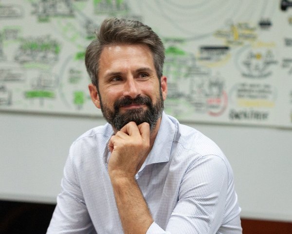 Porträt von Tom Klose mit weißem Hemd, der nachdenklich lächelt.